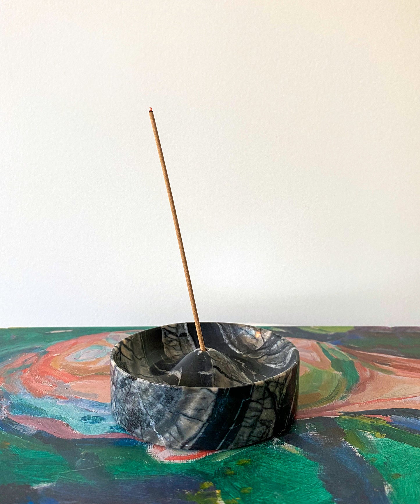 Incense stick in a black marble-like bowl on a colorful abstract background