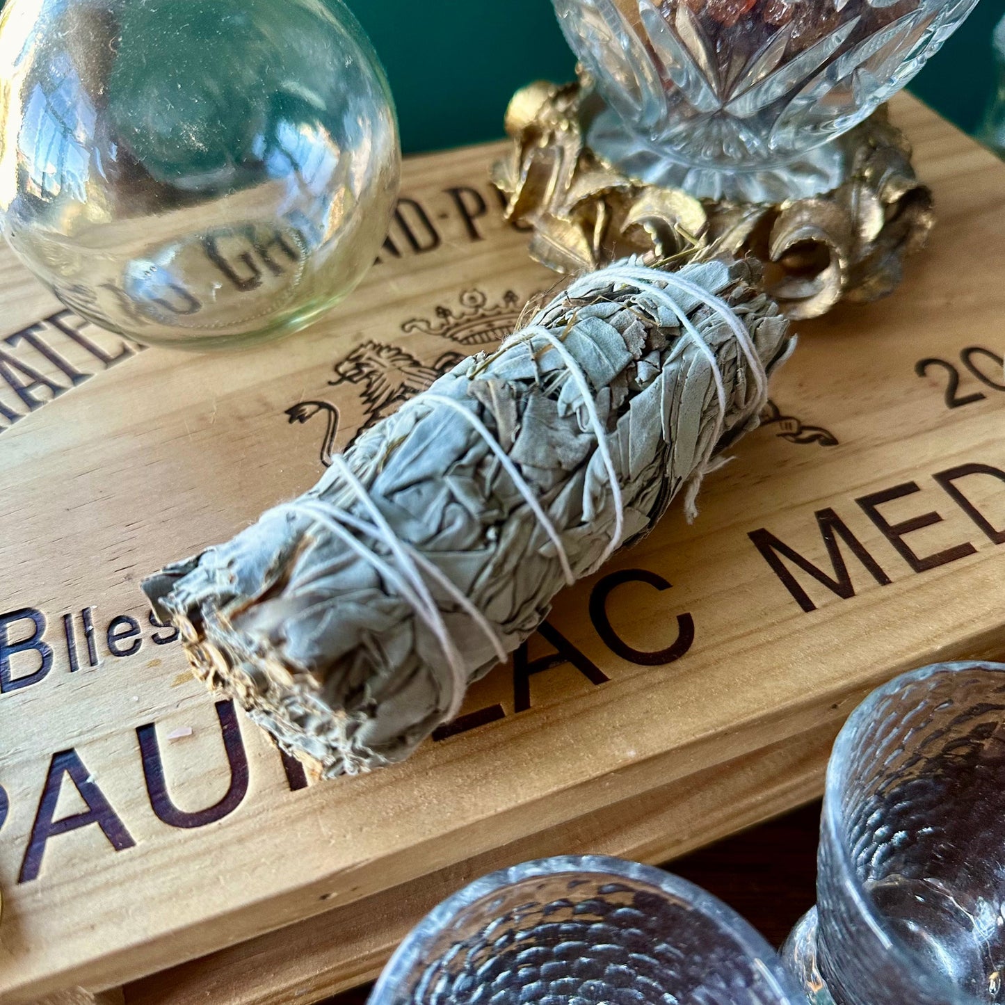 Rolled white sage smudge stick on a wooden surface with glass containers and text.