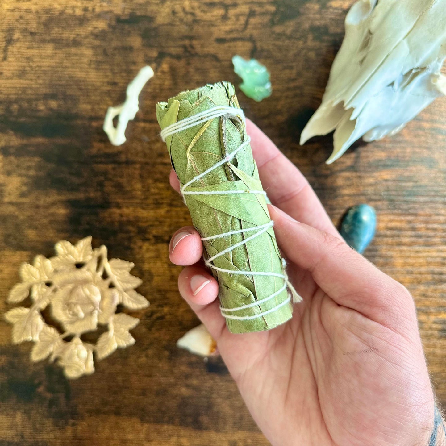 Hand holding a bundle of eucalyptus sage wrapped with white string on a wooden surface.