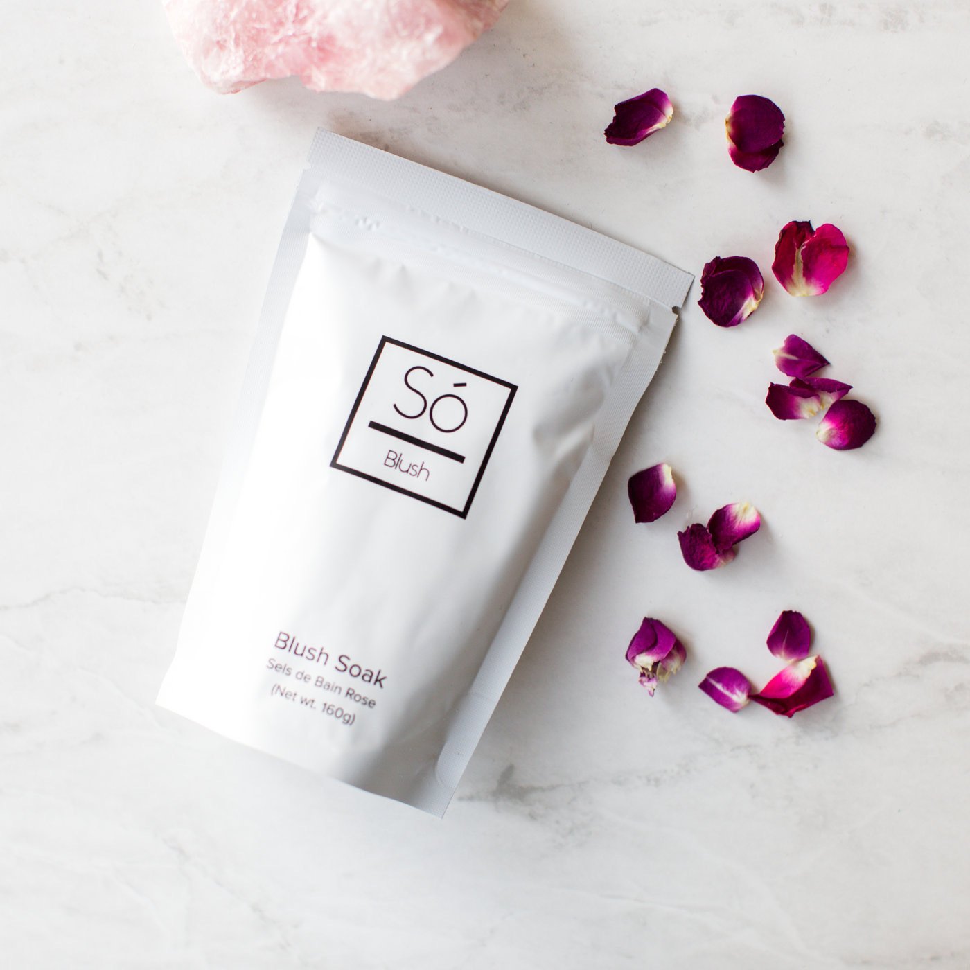 Blush Sóak - Bath Soak on a marble surface with pink flowers and petals.