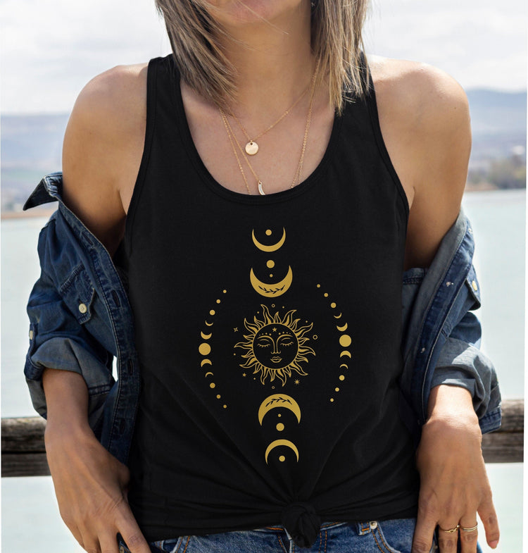 Woman wearing black tank top with gold sun and moon phases graphic design and layered necklaces by water