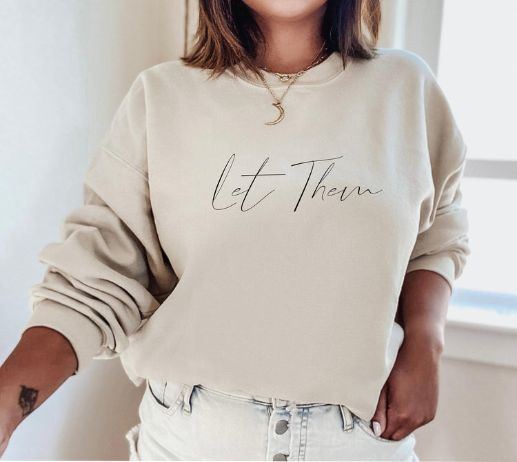 Woman wearing beige Let Them sweatshirt with crescent moon necklace in bright natural light