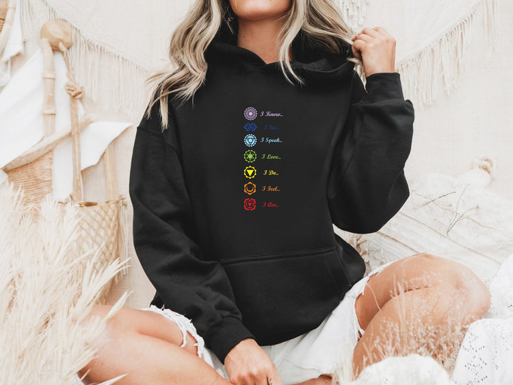 Woman wearing black hoodie with seven chakra symbols and affirmations in cozy bohemian setting