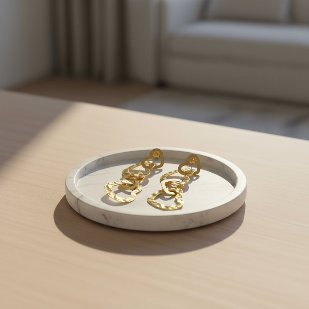 Pair of gold sculptural wavy hoop earrings on minimalist white ceramic jewelry dish