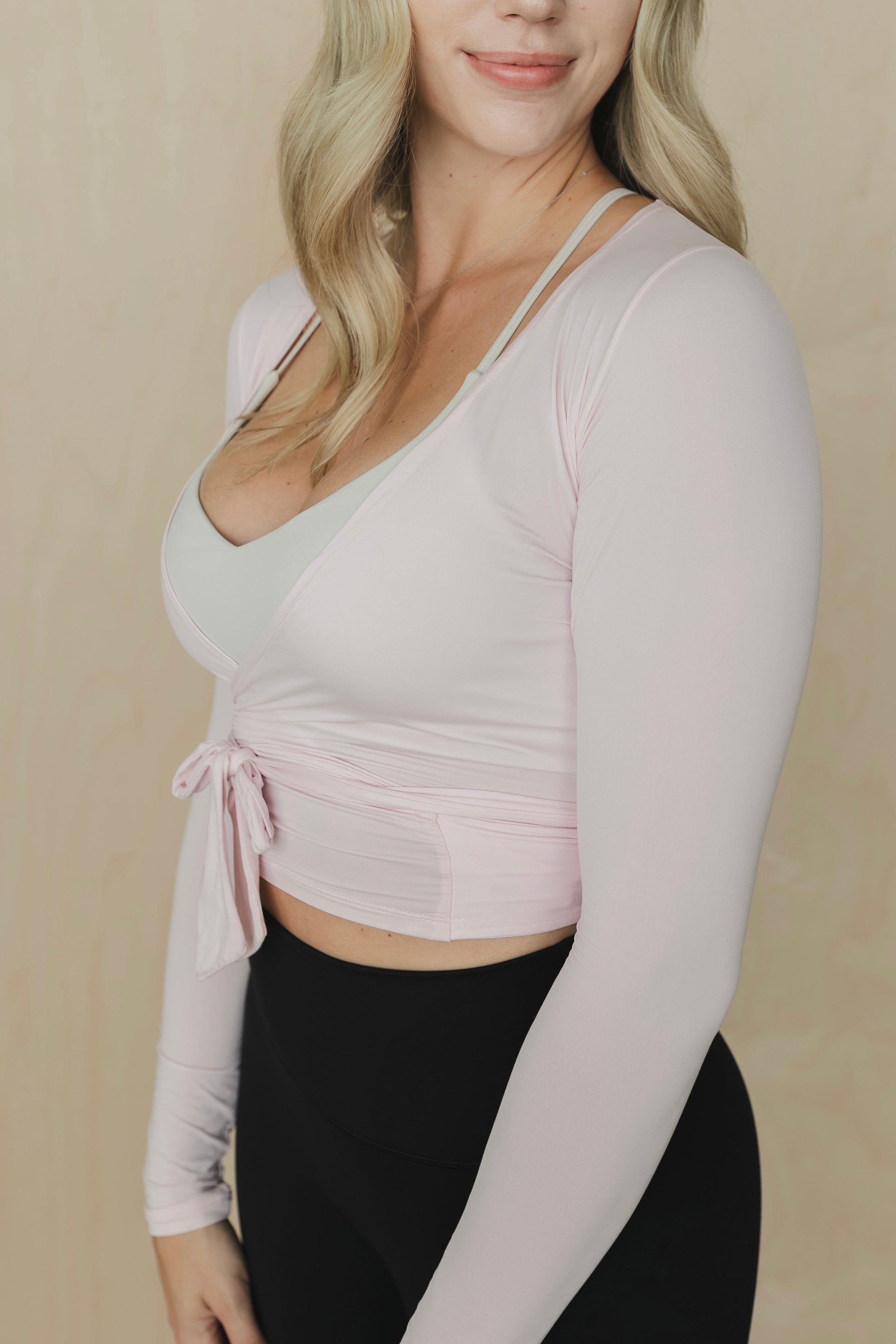 Woman wearing a light pink long-sleeve top and black leggings against a beige background
