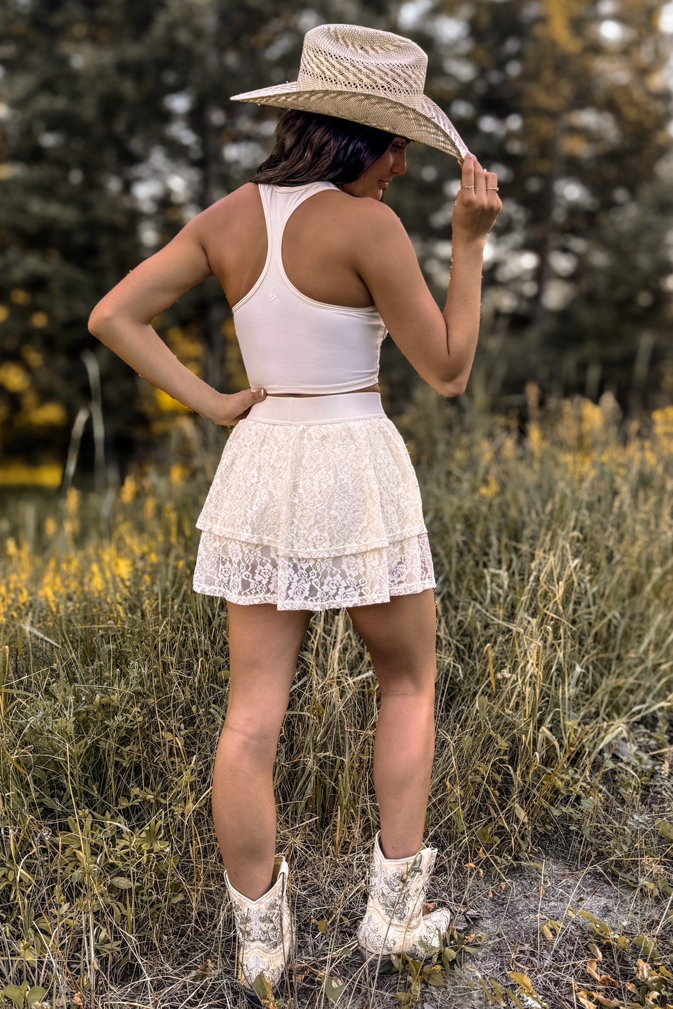 back view of woman wearing a stampede lace active skirt with built-in shorts in cream ivory for festivals and activewear