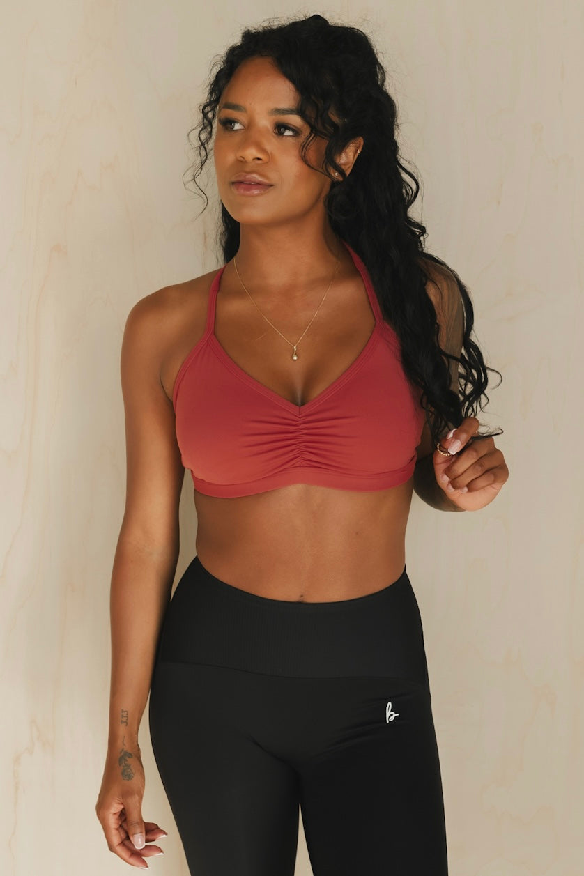zoomed out front view of a woman wearing a mini scrunch bra in garnet for yoga and studio workouts