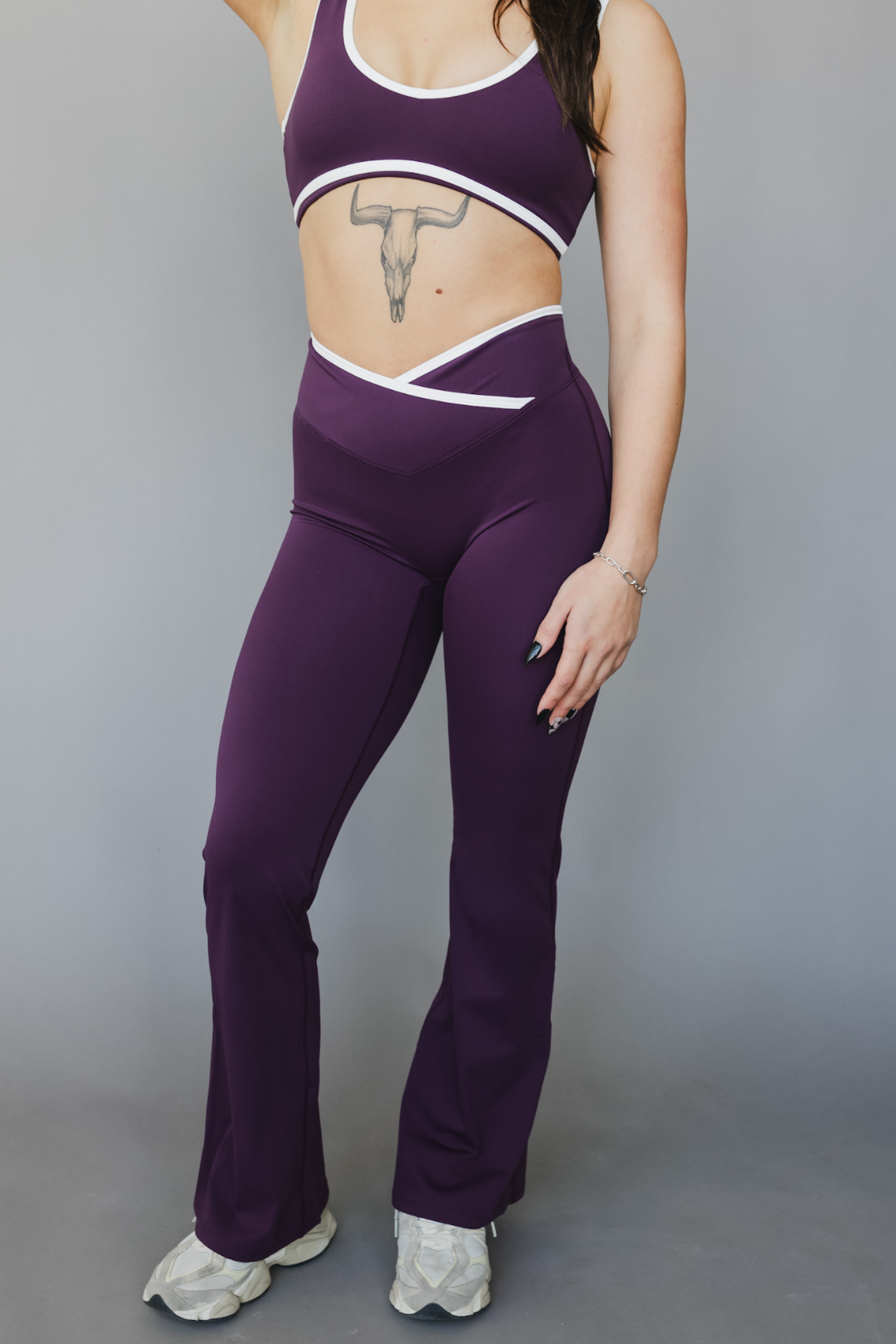 front view of a woman wearing flare leggings in eggplant purple with white trim for workouts and casual athleisure