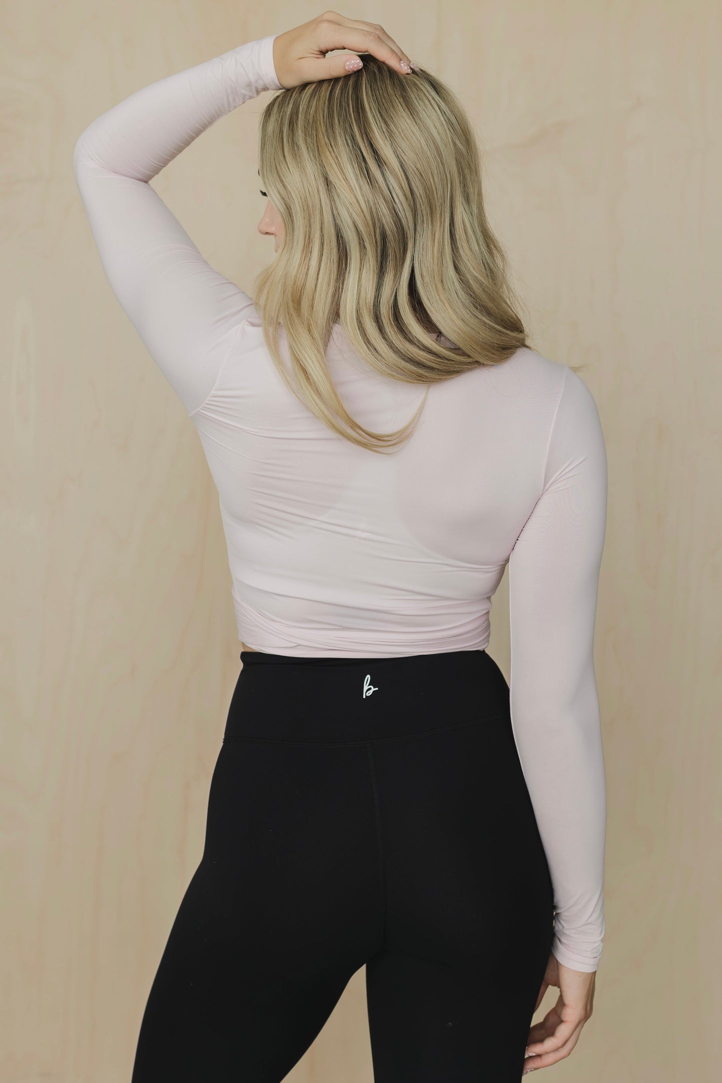 Person wearing a light pink long-sleeve top and black leggings against a beige background