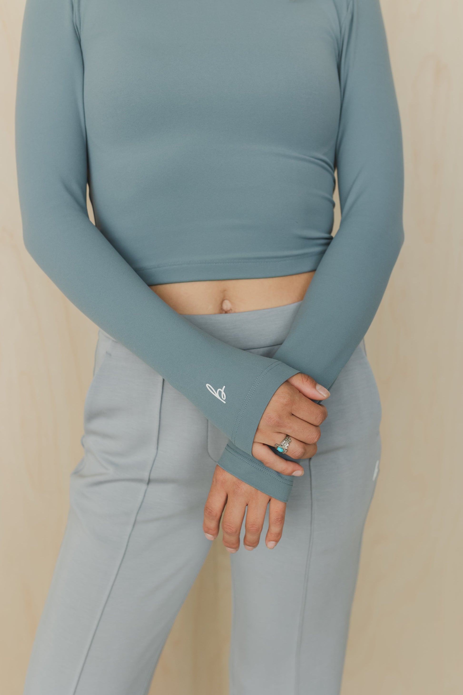 mid section view of a woman wearing a blue long-sleeve top and gray leggings on a beige background