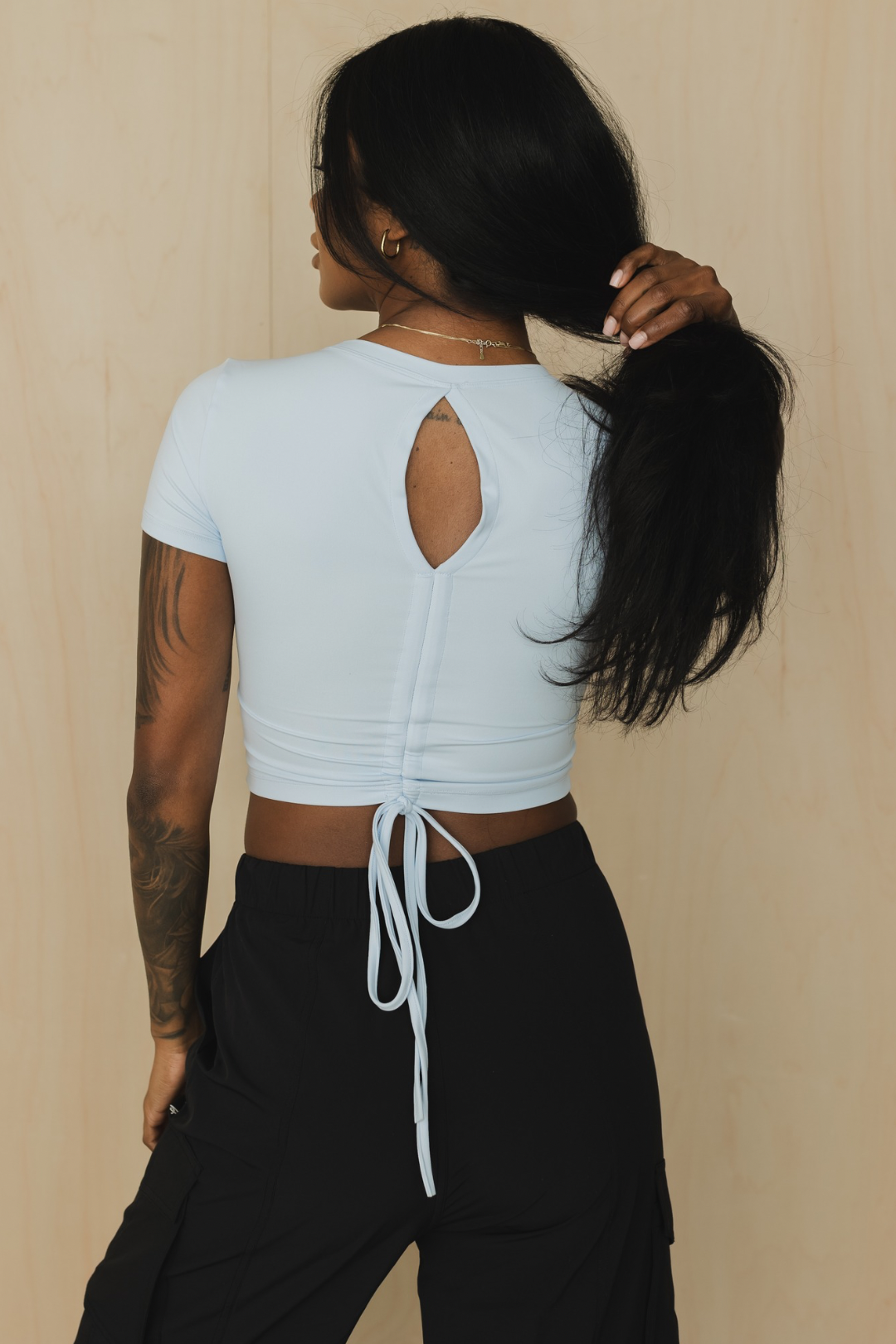 back view of a person wearing a light blue crop top with an open back and black pants against a beige background