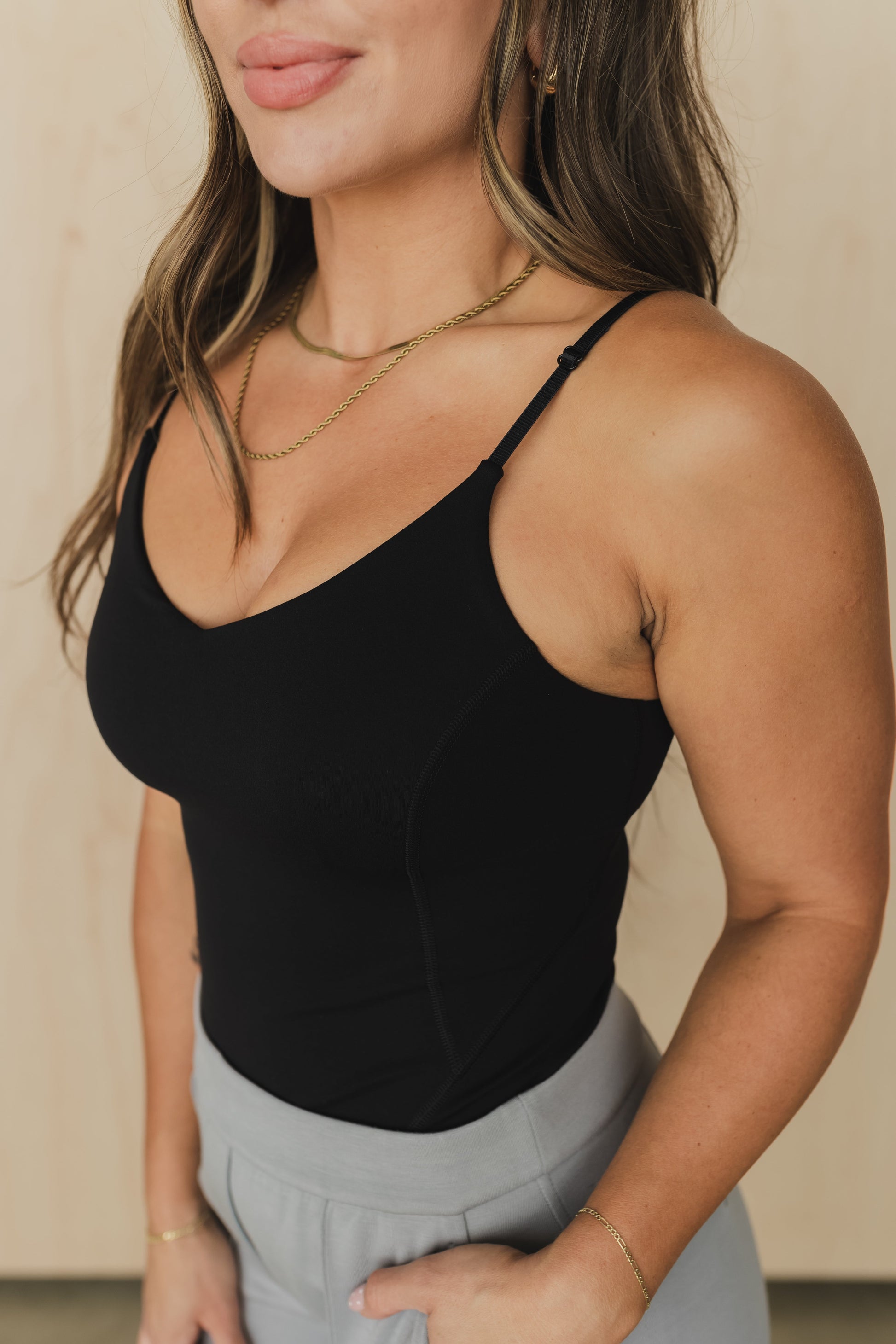 Woman wearing a black tank top and light gray pants against a neutral background