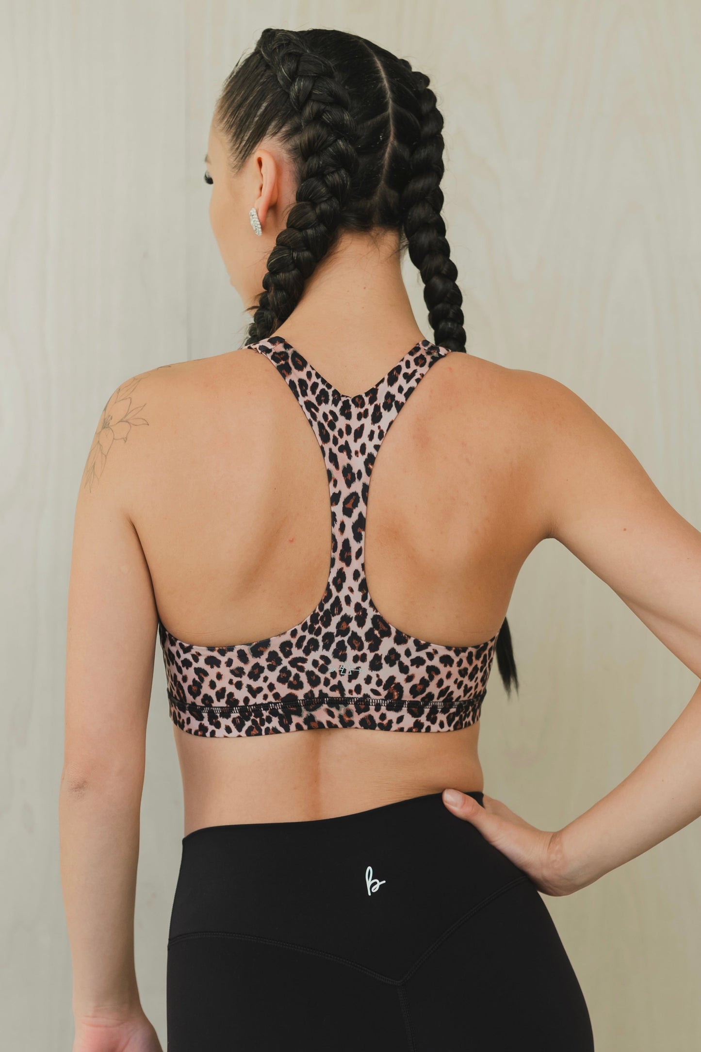 back view of a woman wearing a minimalist sports bra in leopard print with black pants for yoga and studio workouts