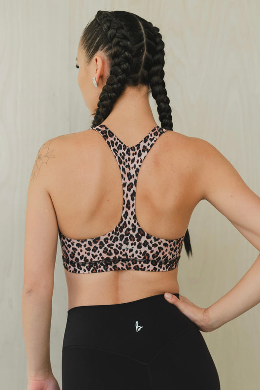 back view of a woman wearing a minimalist sports bra in leopard print with black pants for yoga and studio workouts