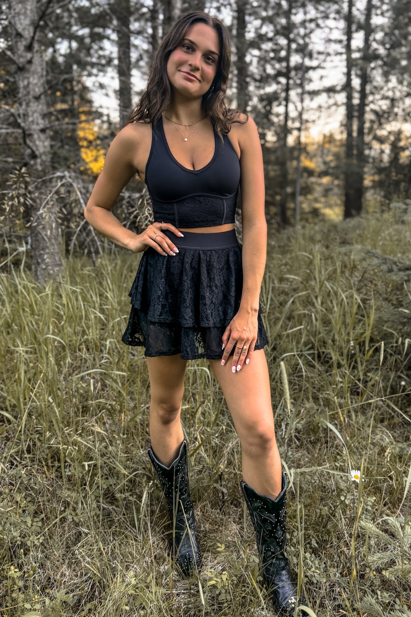front view of woman wearing a stampede lace active skirt with built-in shorts in black along with cowboy boots dressed for festivals and activewear