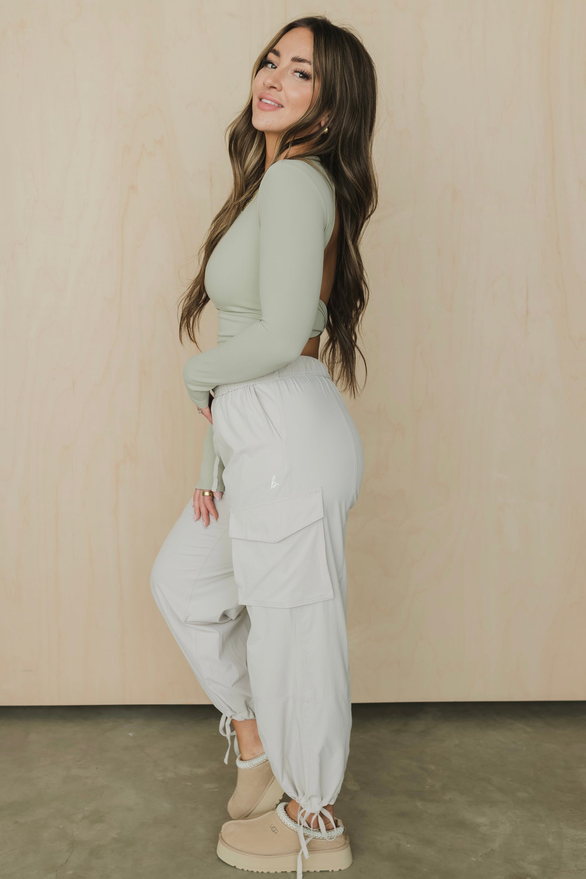 Woman wearing a green top and light gray pants against a beige wall.