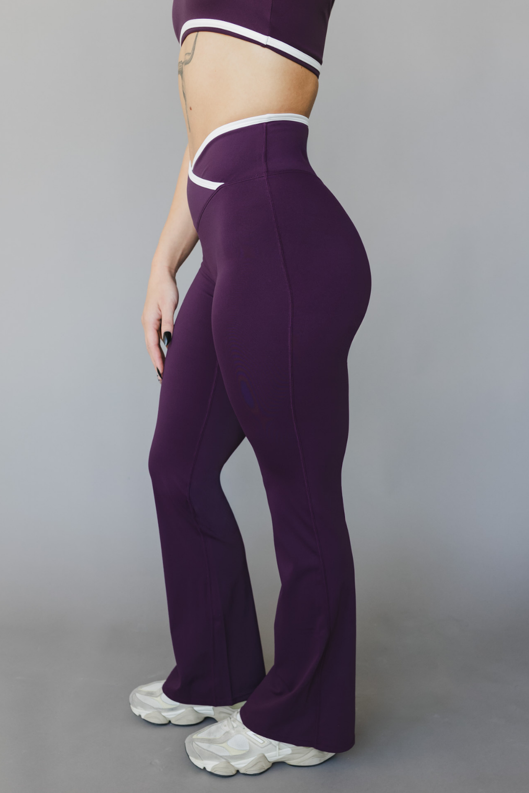 side view of a woman wearing flare leggings in eggplant purple with white trim for workouts and casual athleisure