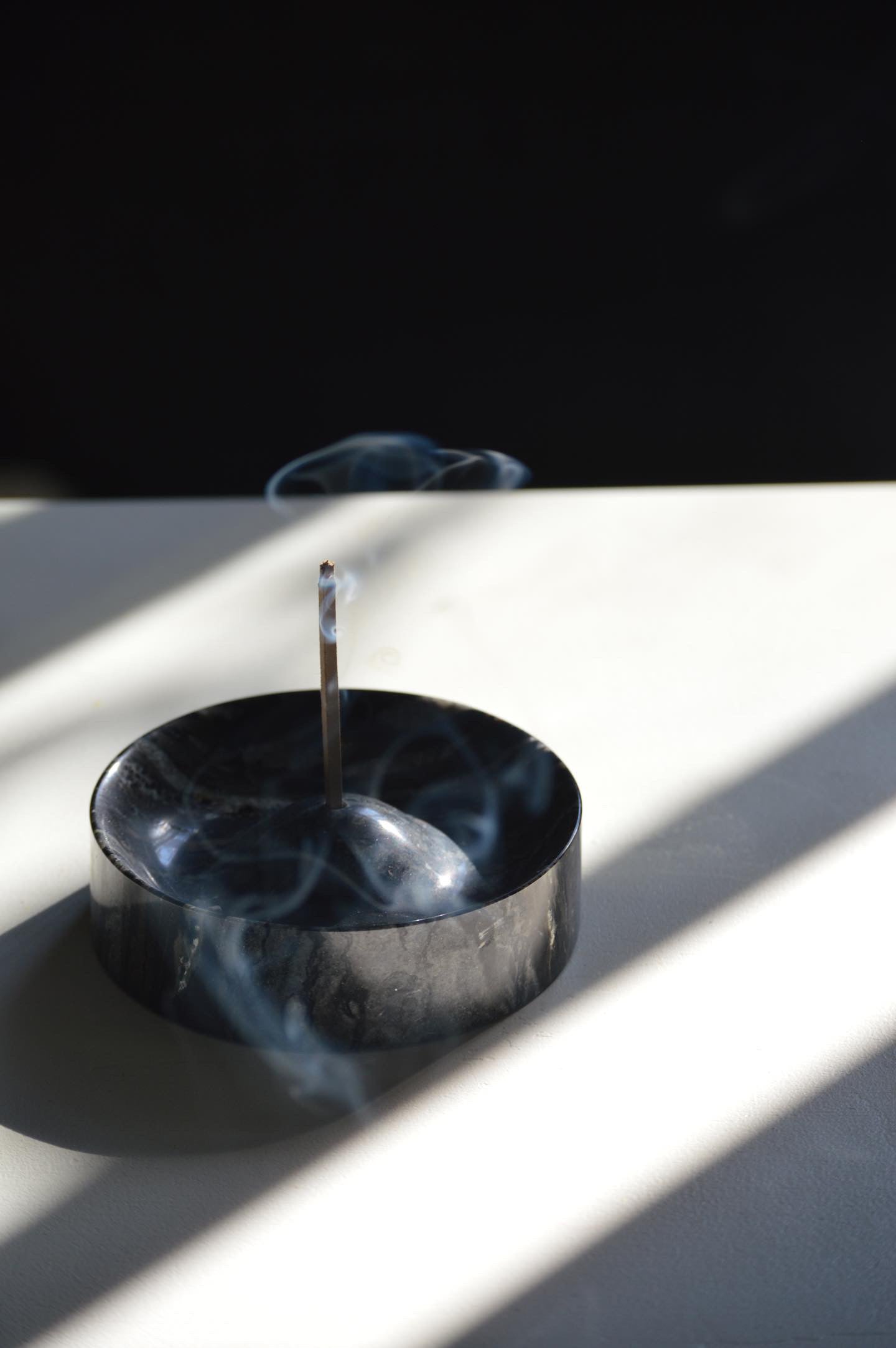 Black incense burner with smoke on a white surface with black background