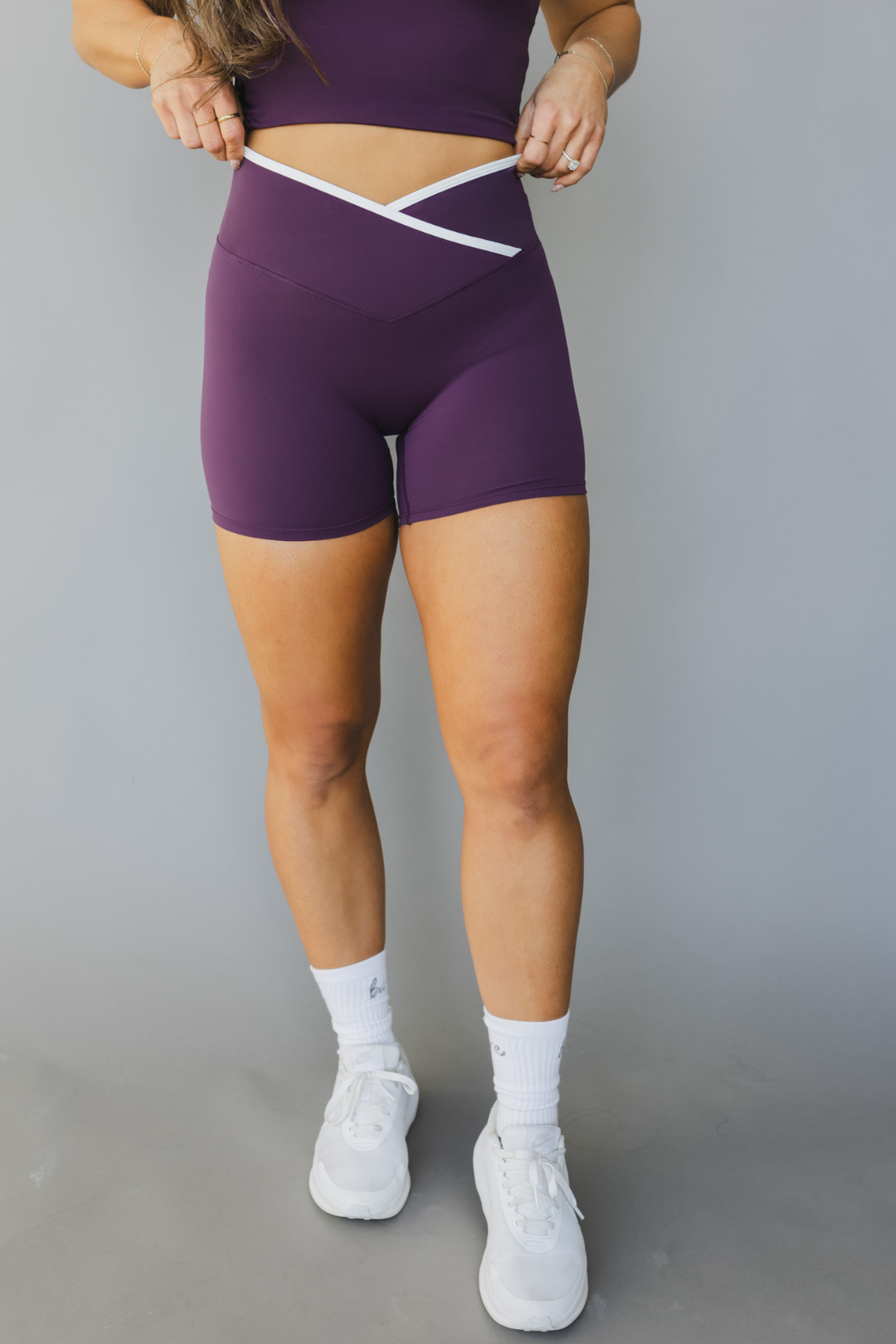 front view of a woman wearing Tina shorts in eggplant purple with white trim and a matching tank top for athletic wear and loungewear