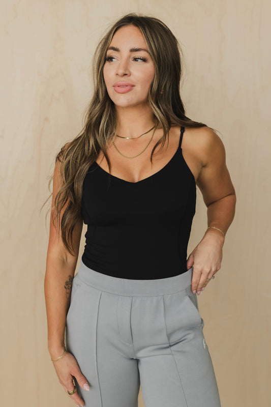 Woman wearing a black tank top with built in bra and light gray pants against a beige background