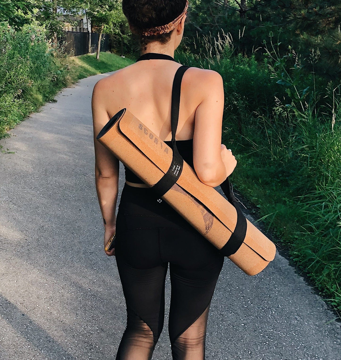woman carrying Cork yoga mat with moon phase design down a walking path outside
