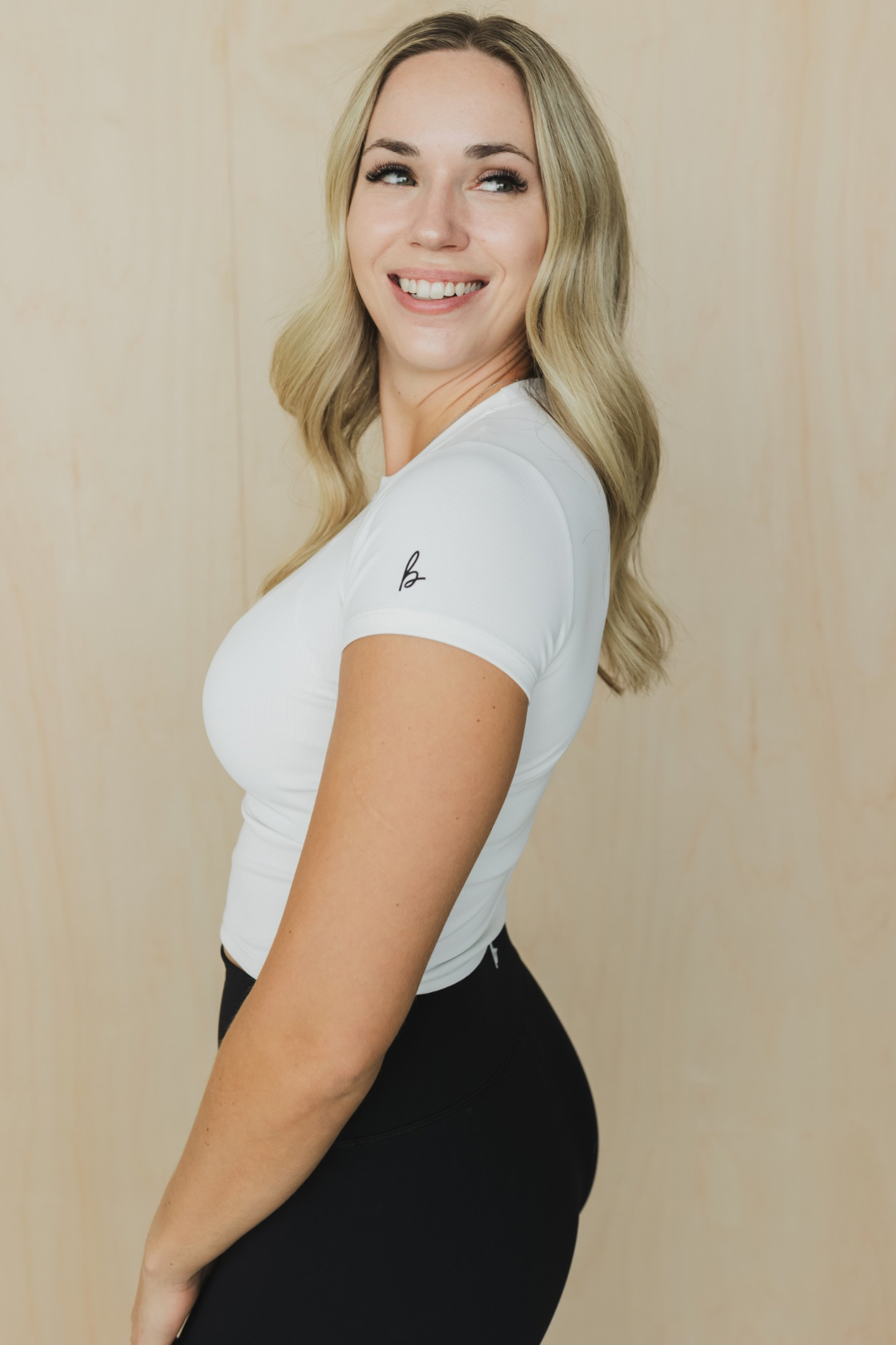 Woman wearing a white t-shirt with a logo against a beige background