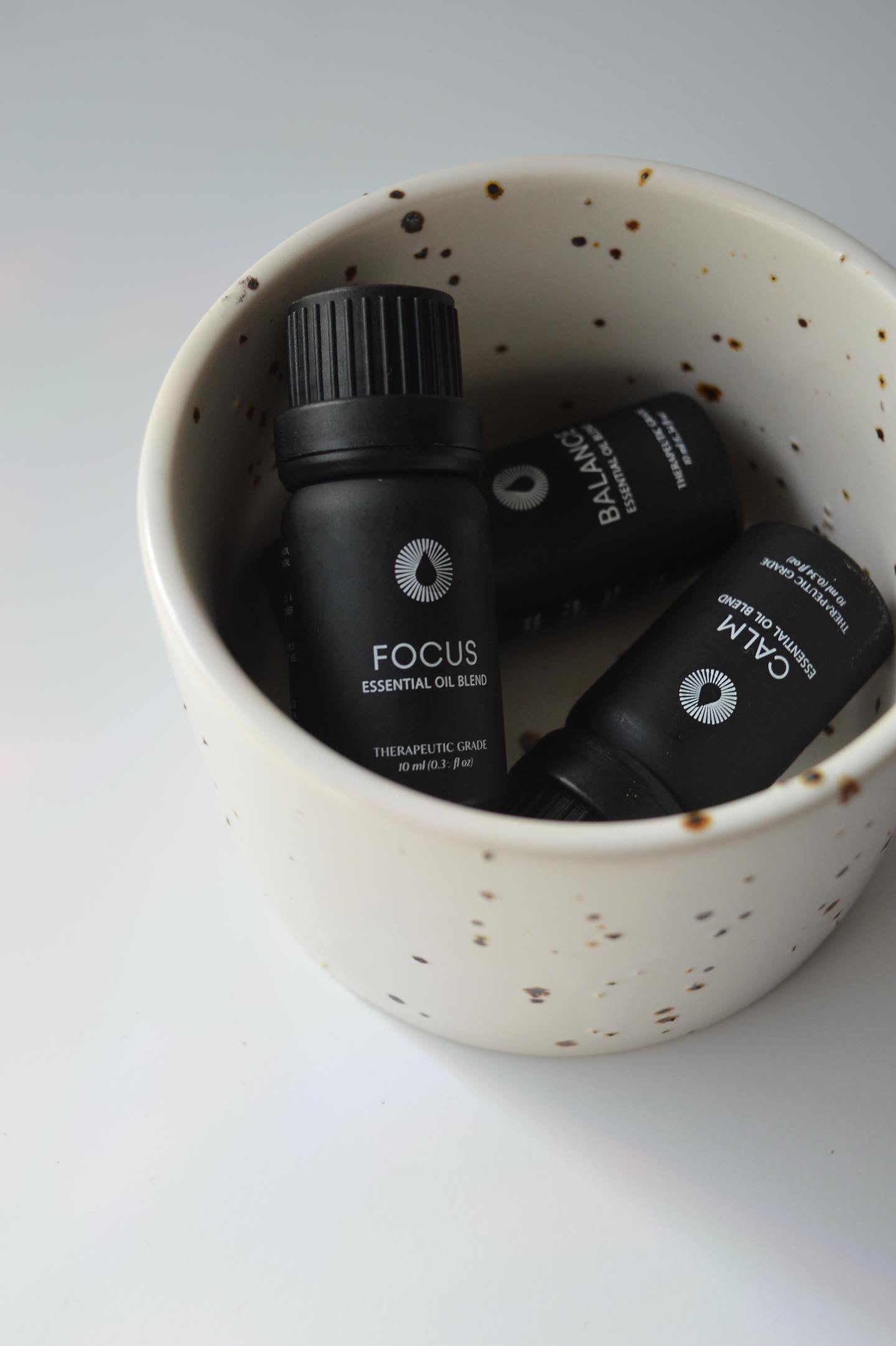 Three black essential oil bottles labeled 'Focus', 'Balance', and 'Calm' in a speckled ceramic bowl.