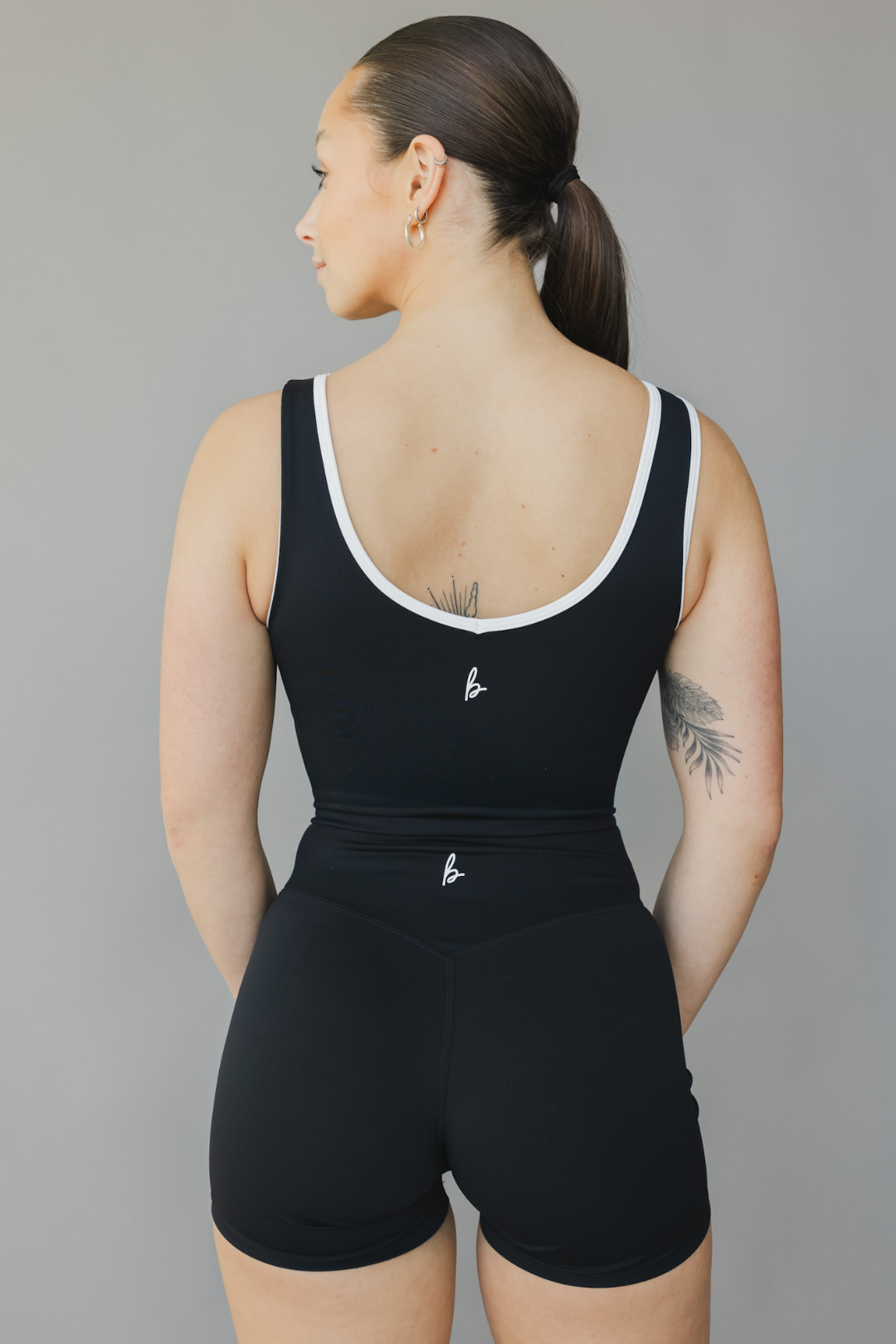 back view of a person wearing a black athletic tank top with white trim and matching shorts on a gray background