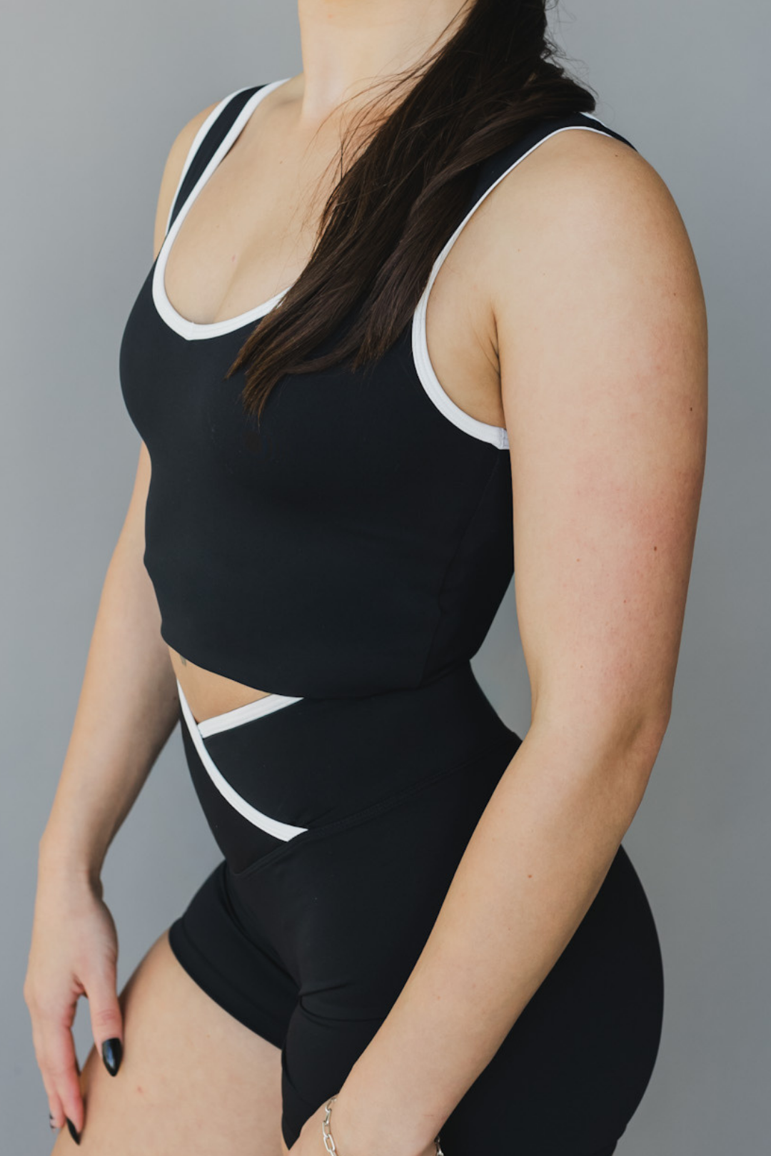 Person wearing a black sports bra and shorts with white trim on a gray background