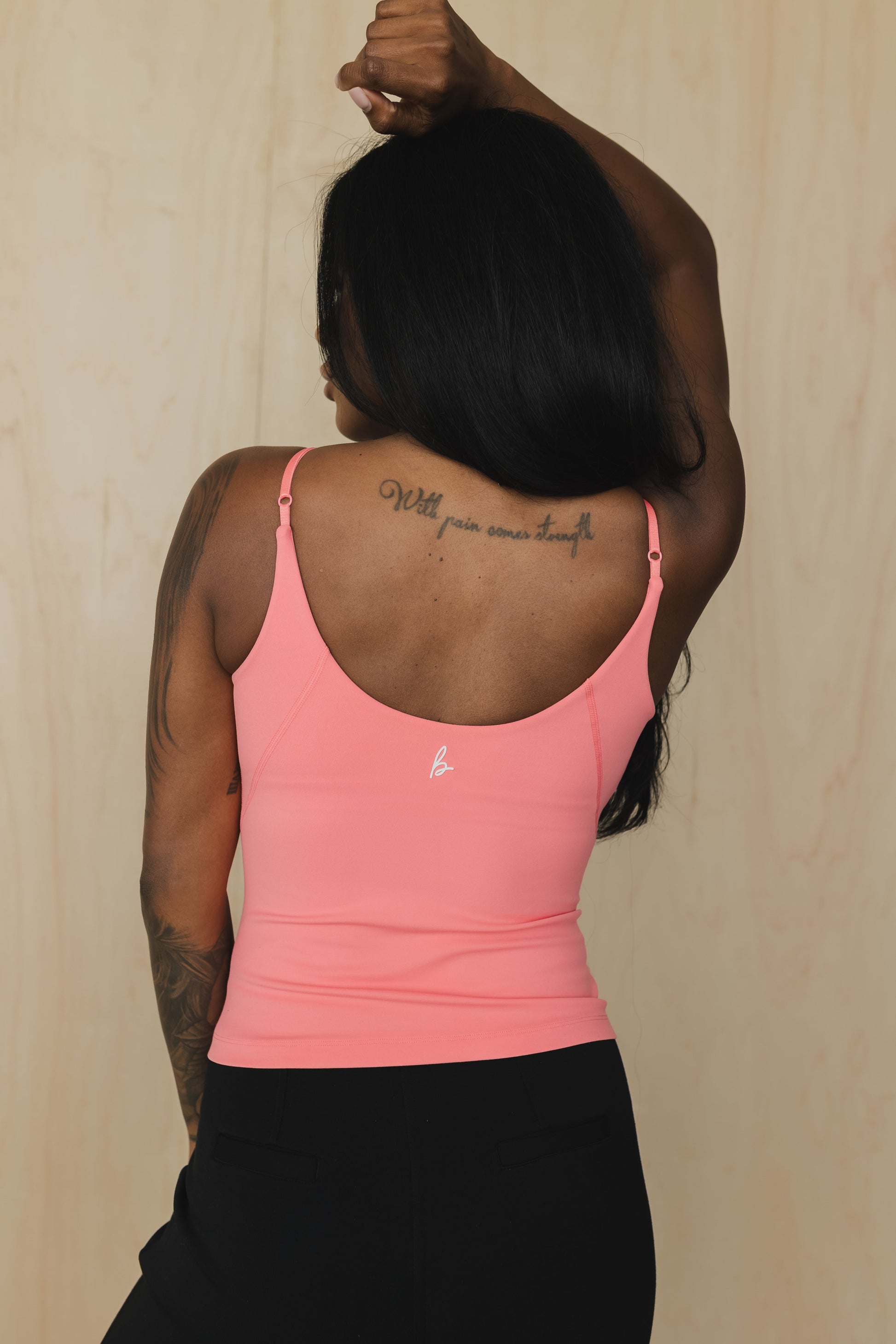 close up back view of a woman wearing a light pink tank top with built in bra and light gray pants against a beige background