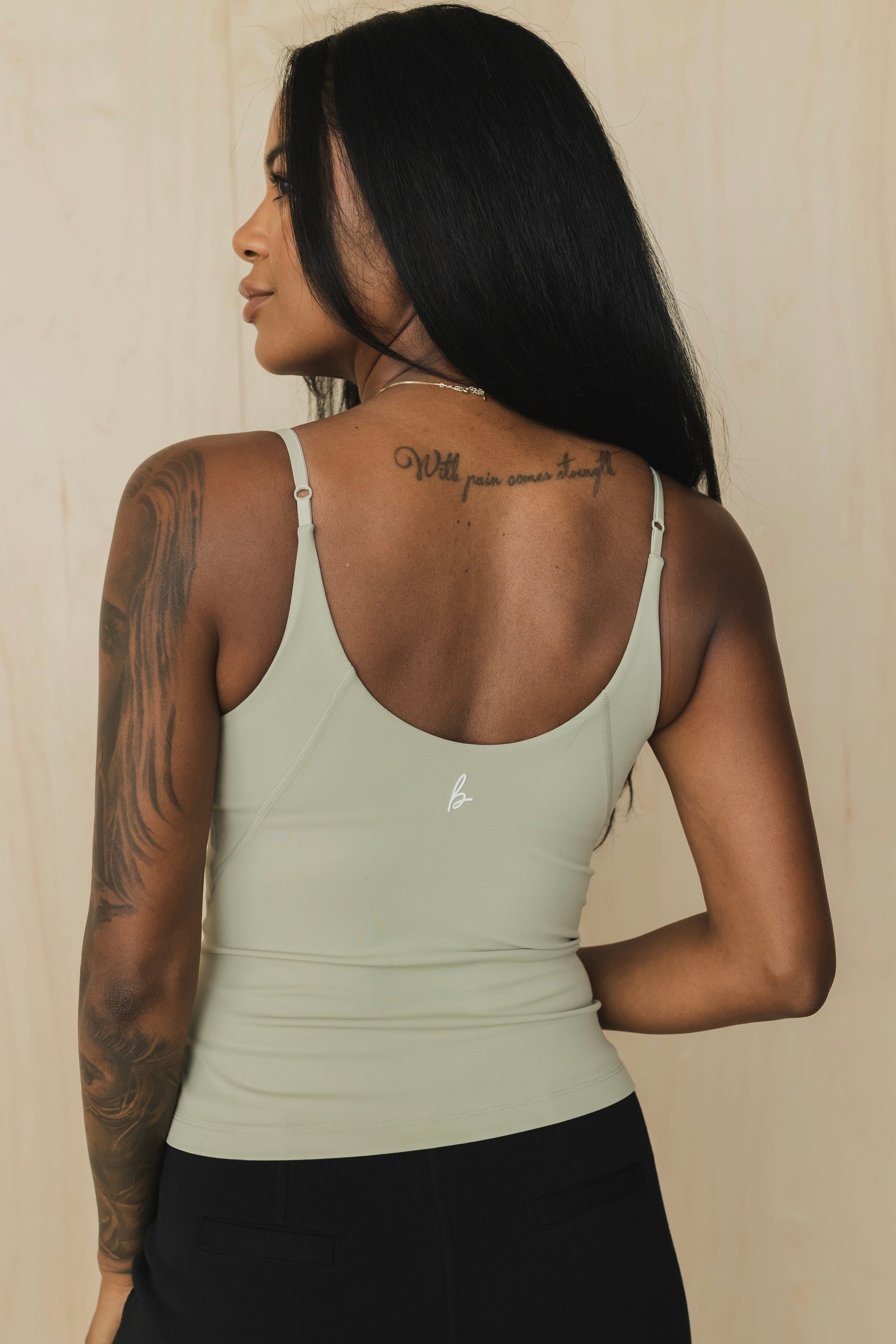 close up back view of a woman wearing a light green tank top with built in bra and light gray pants against a beige background