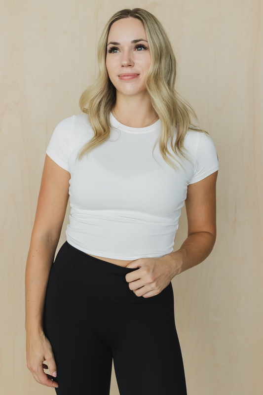 Woman wearing a white crop top and black pants against a beige background