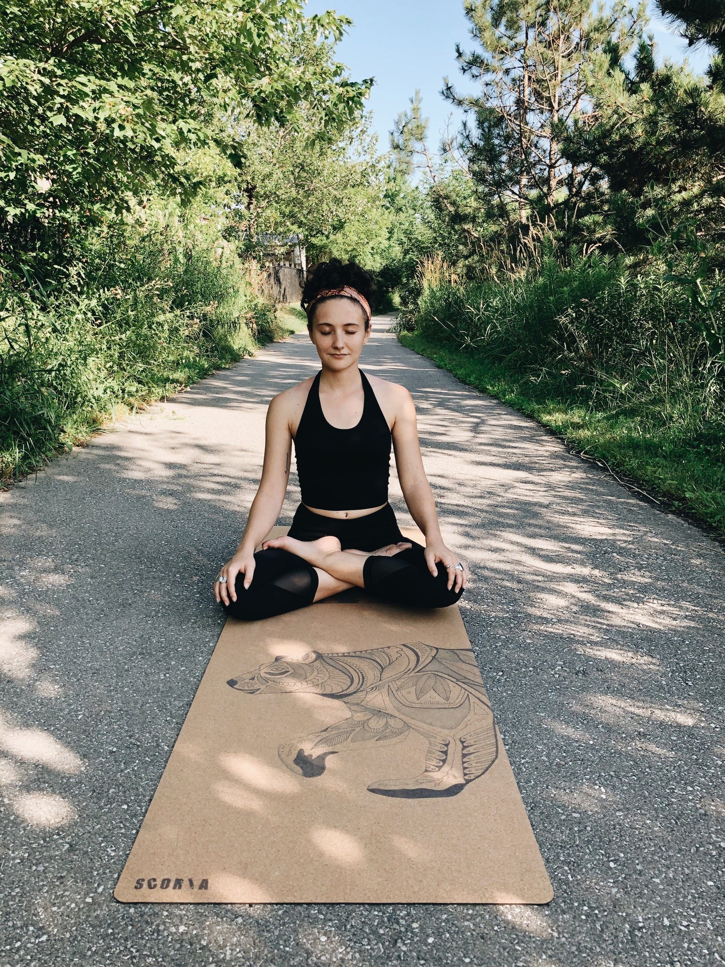 Person sitting on a bear-patterned yoga mat outdoors in a natural setting