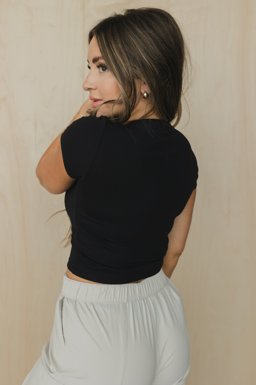 Back view of a woman wearing a black crop top and light gray pants against a beige background