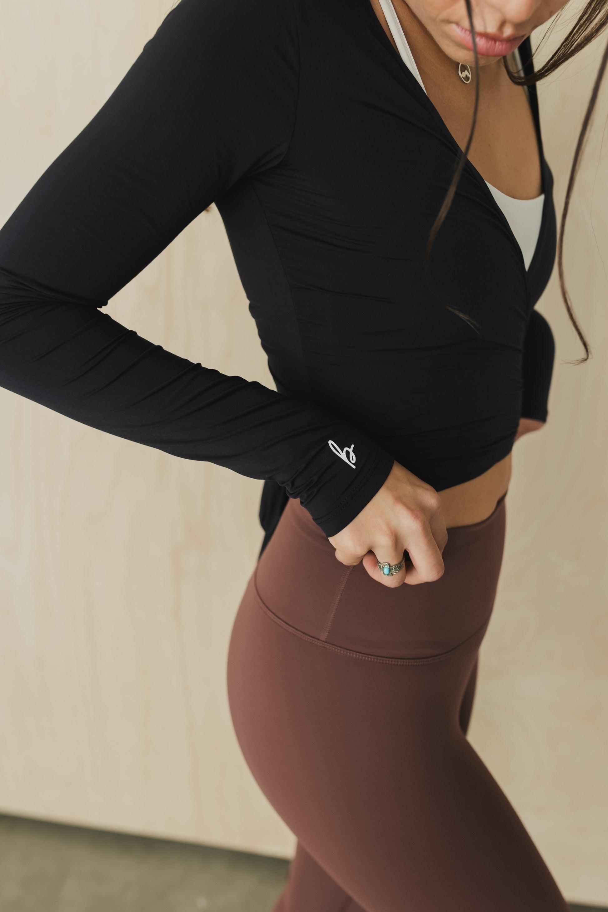Person wearing a black long-sleeve top and brown leggings against a neutral background