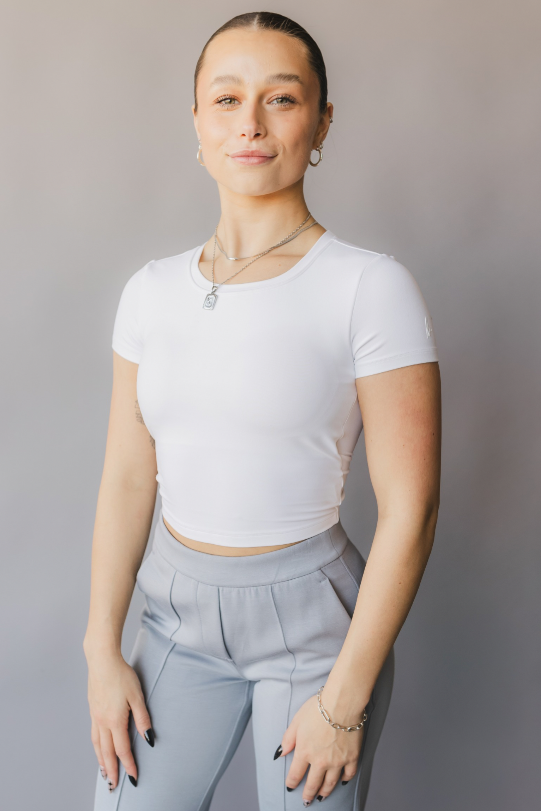 front view of a woman wearing a white crop top with cut-out design and light gray pants against a beige background