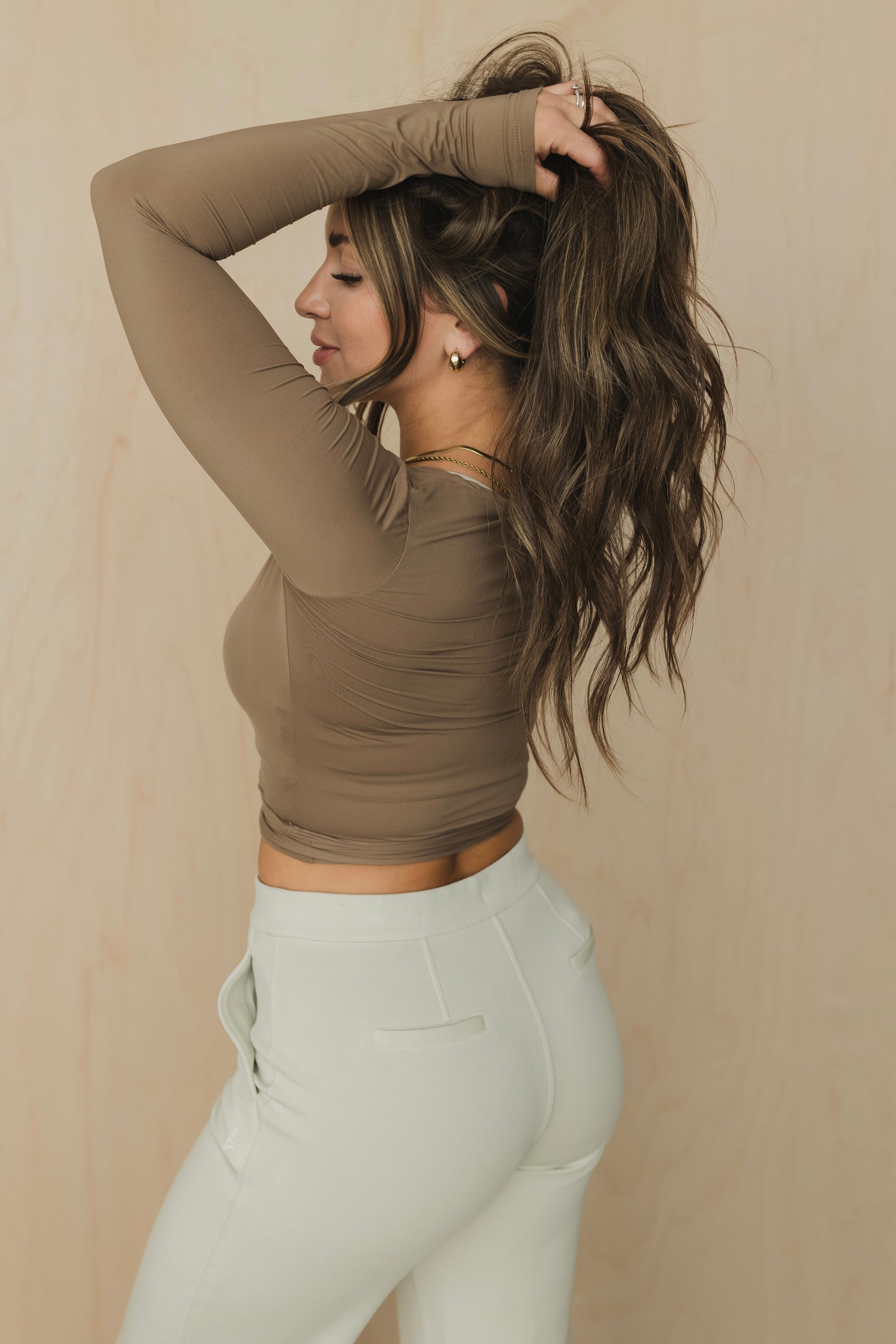 Woman wearing a brown long-sleeve top and light gray pants against a beige background
