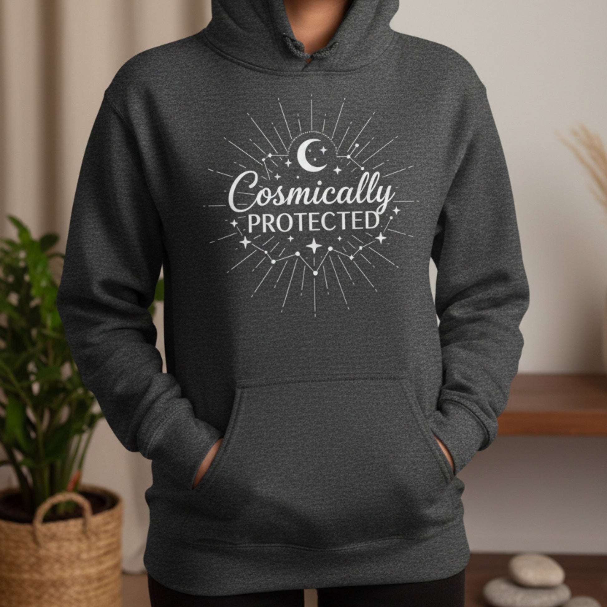 Dark heather gray cosmically protected hoodie with white sunburst and crescent moon graphic — cozy celestial gift for the spiritual woman who finds warmth in knowing she is guided