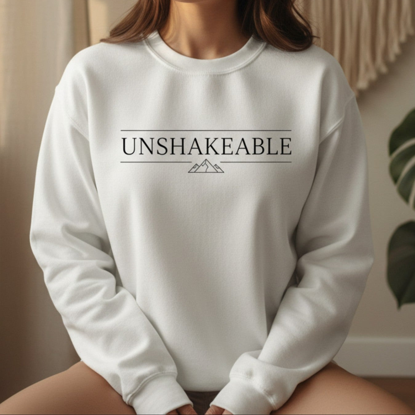 White Unshakeable crewneck sweatshirt with black serif wordmark and mountain print — empowerment gift for the woman who has been tested by life and proven she cannot be moved