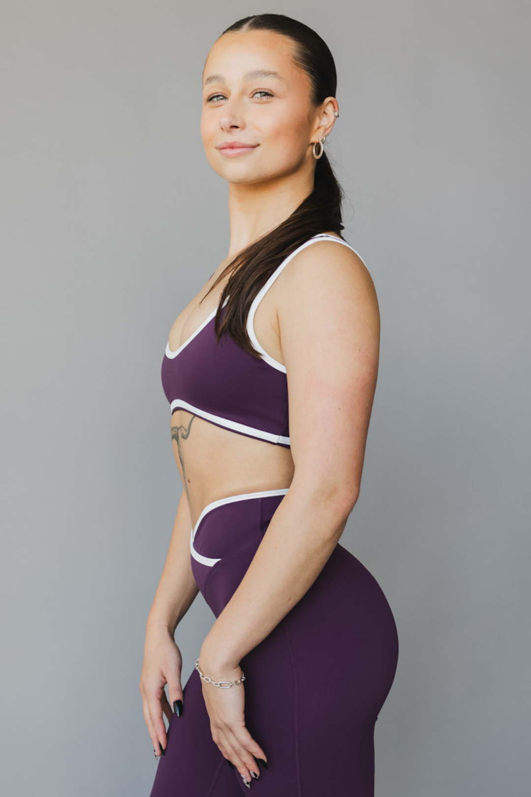 side view of a woman wearing a tina sports bra with white trim and scoop neckline in eggplant purple for yoga and fitness