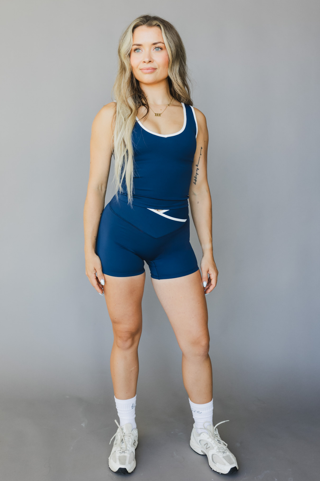 full lengh front view of a person wearing a blue color athletic tank top with white trim and matching shorts on a gray background