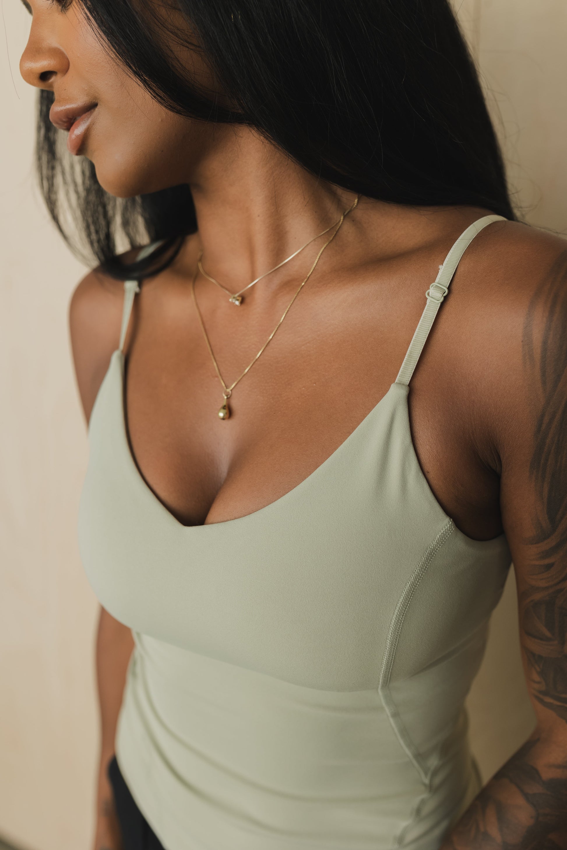 close up front view of a woman wearing a black tank top with built in bra and black pants against a beige background