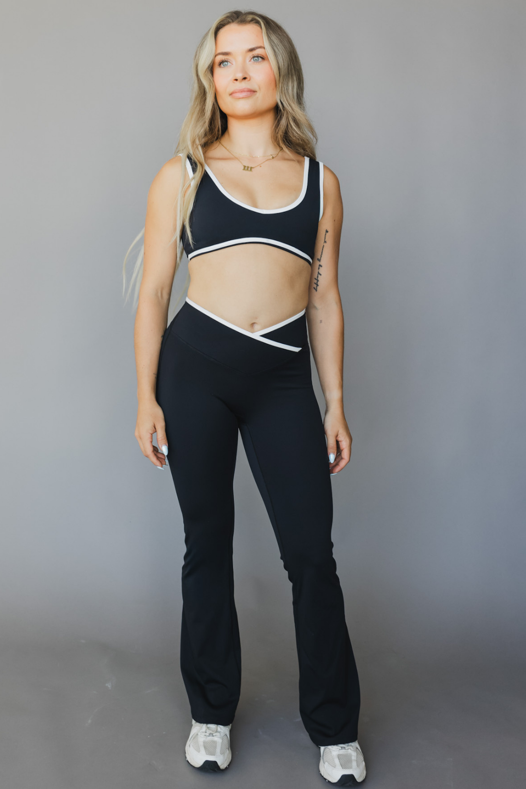 full body view of a woman wearing flare leggings in black with white trim for yoga and studio wear