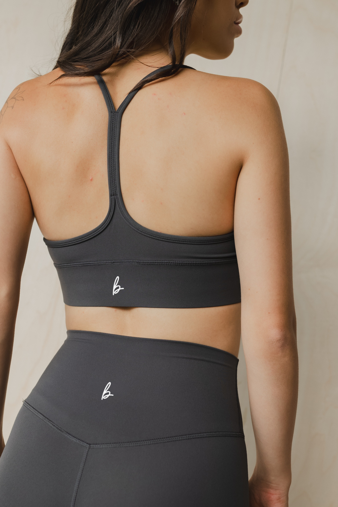 Person wearing a dark grey sports bra and leggings with a visible brand logo on a neutral background