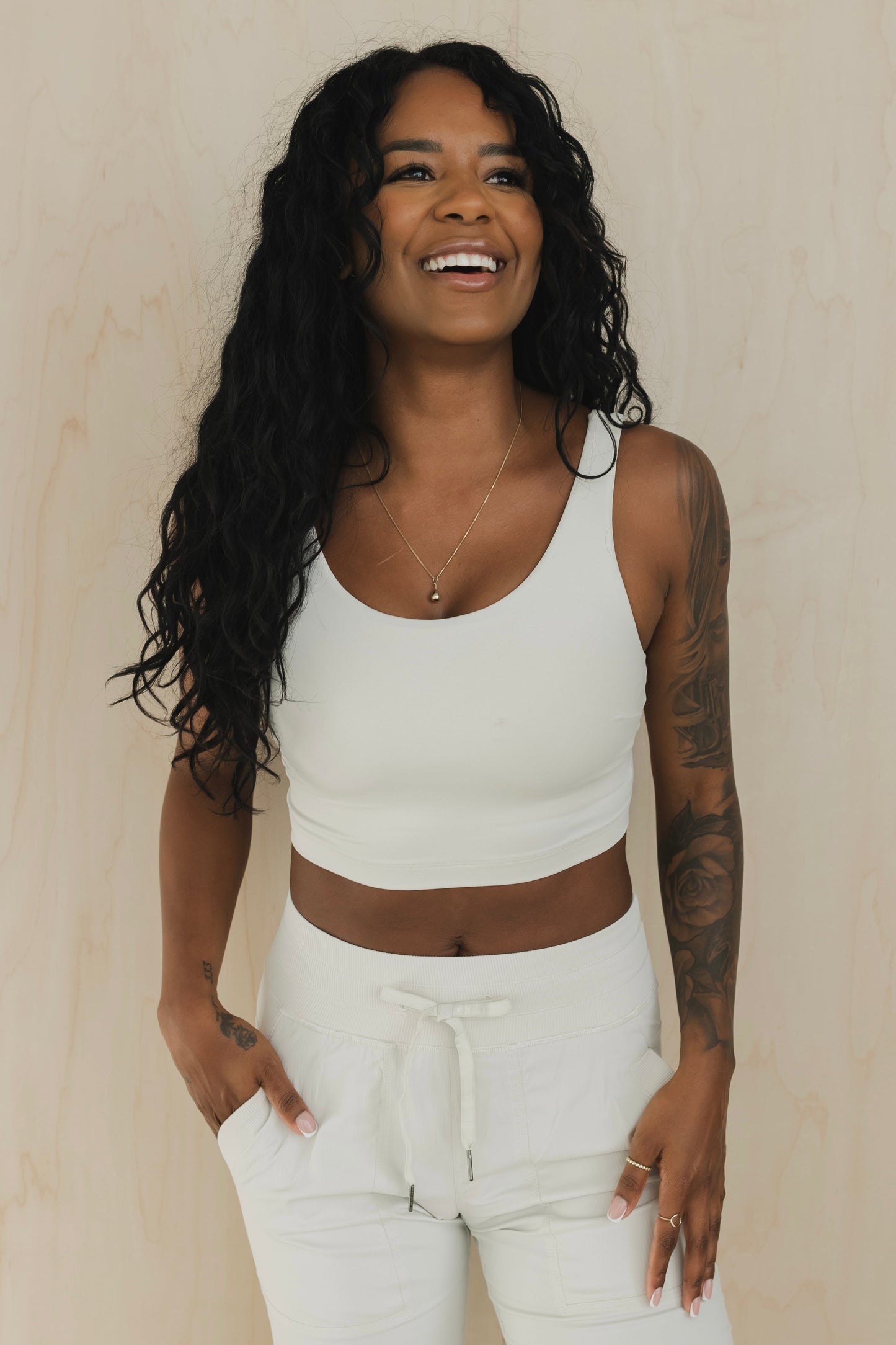 front view of a woman laughing wearing wrap back sports bra in buff beige for yoga and fitness