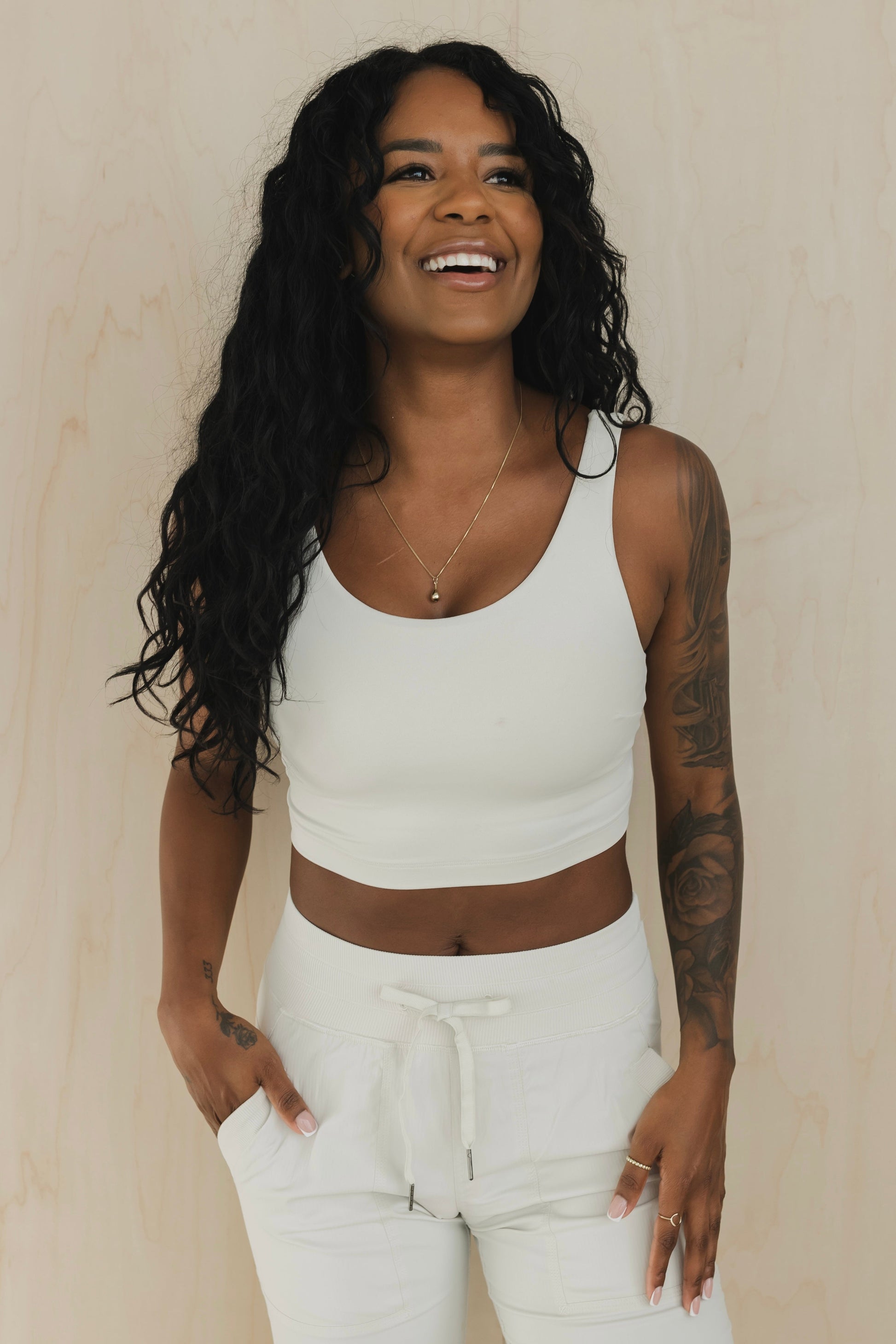 front view of a woman laughing wearing wrap back sports bra in buff beige for yoga and fitness