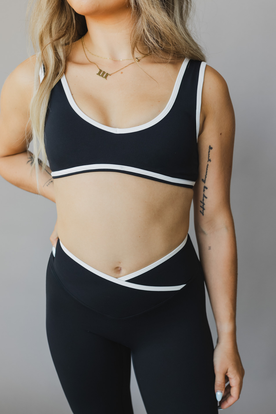 front view of a woman wearing a tina sports bra with white trim and scoop neckline in black for yoga and fitness