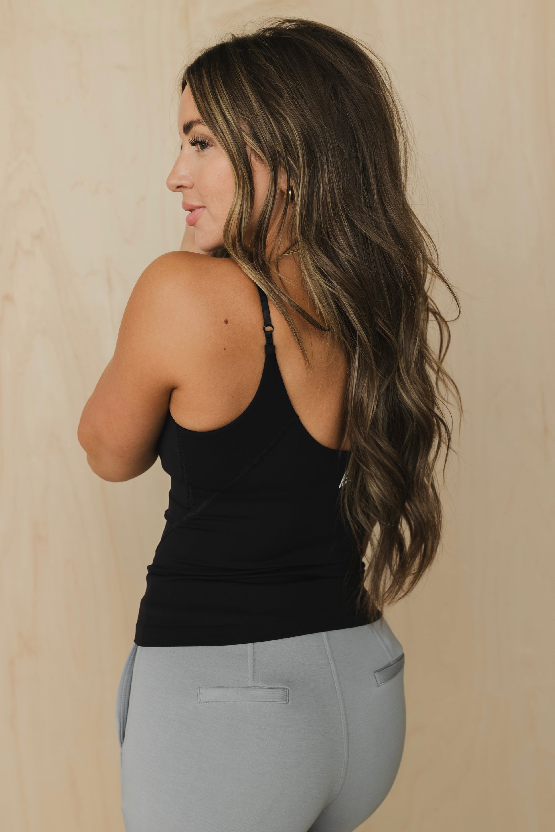 Woman wearing a black tank top and gray leggings against a beige background