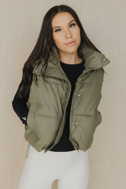 front view of woman wearing a cropped faux leather puffer vest in sage for layering and casual wear