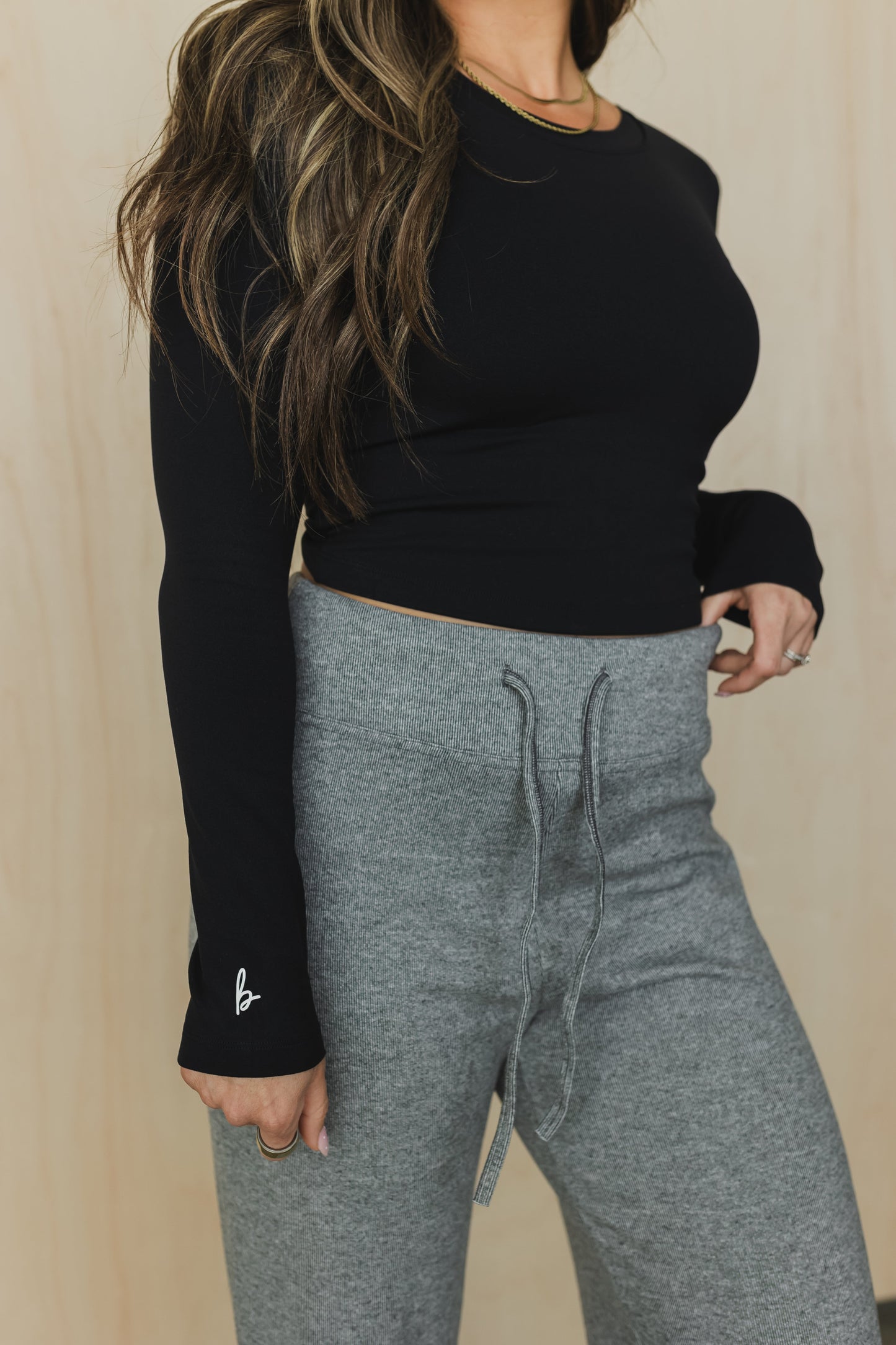 Person wearing a black long-sleeve top and gray sweatpants against a beige background